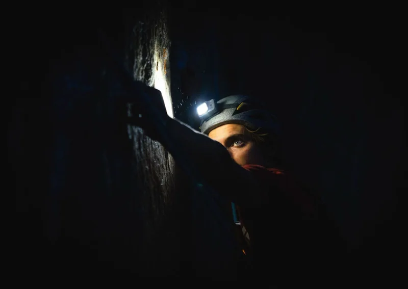 A person climbing in the dark with a headlamp.