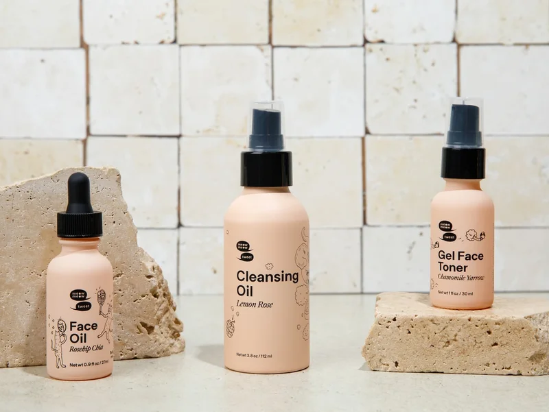 Three pink bottles of skincare products arranged against slabs of marble.