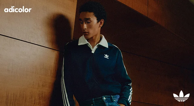 Man with short dark hair wearing navy blue adicolor track jacket and jeans.