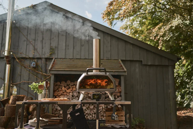 Ooni Karu 2 Pro on a Ooni table in a garden, with chopped wood behind