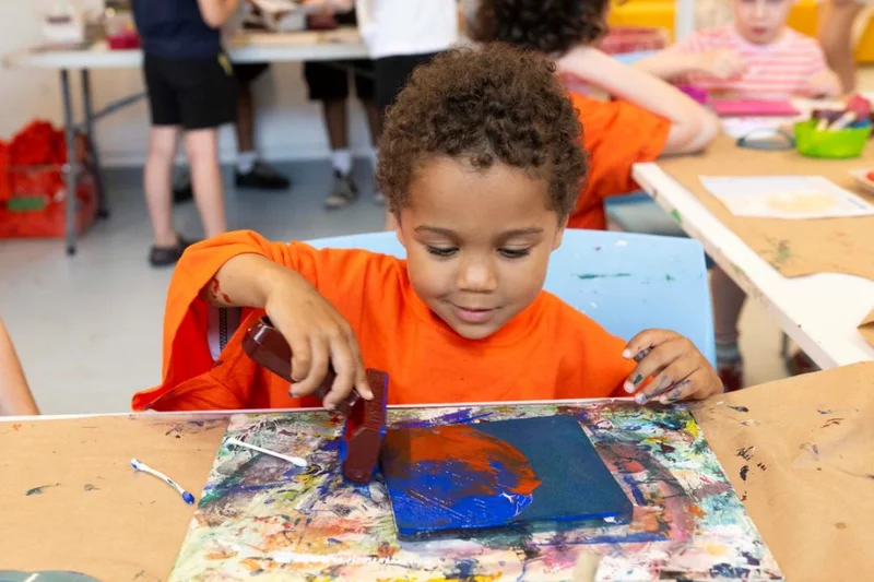 A child in a bright orange shirt makes art with paint