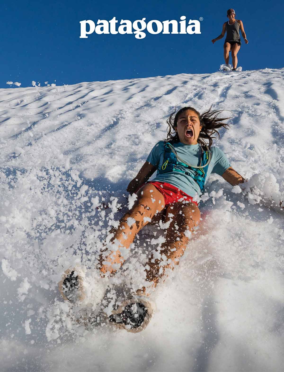 Patagonia. A hiker slides down a snowy slope in shorts and a tee shirt.