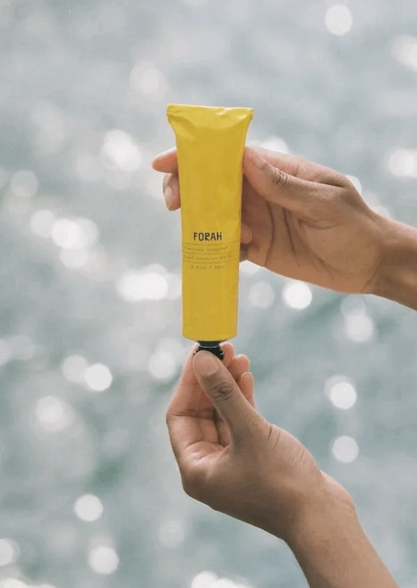 A collection of images of a yellow tube of sunscreen being handled by a person with brown skin