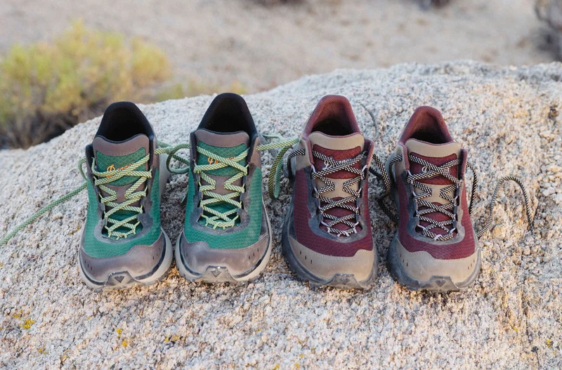 Two pairs of Trail Junction hiking shoes, one in Bracken/Peridot Green and the other in Kangaroo/Chocolate, are displayed side by side on a large desert rock surface.