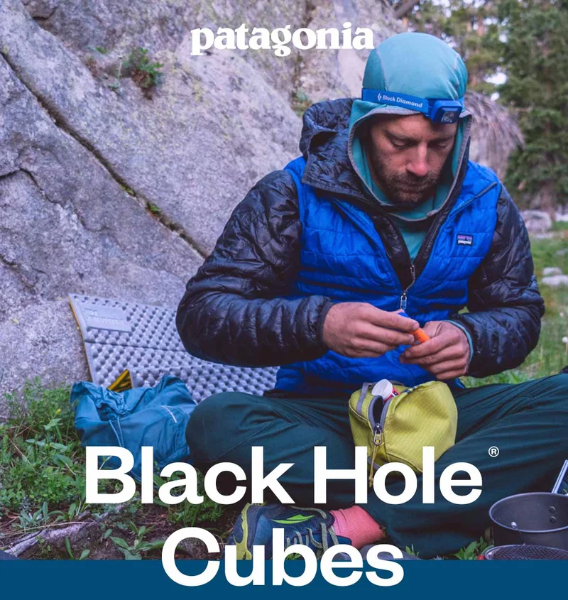 Patagonia. Black Hole Cubes. A person wearing a puffy jacket puts items in a small bag.