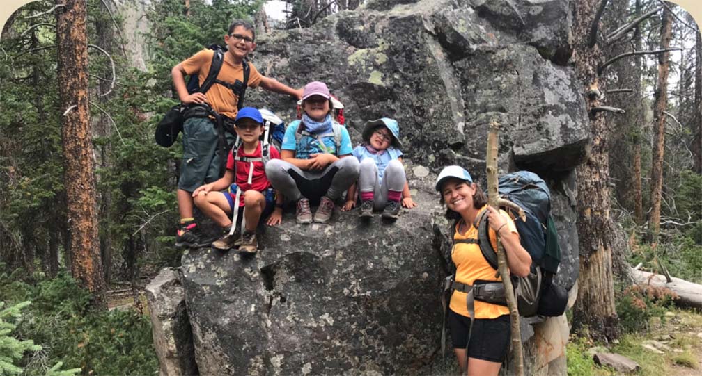 A family of five backpackers pose for a photo on a large boulder.