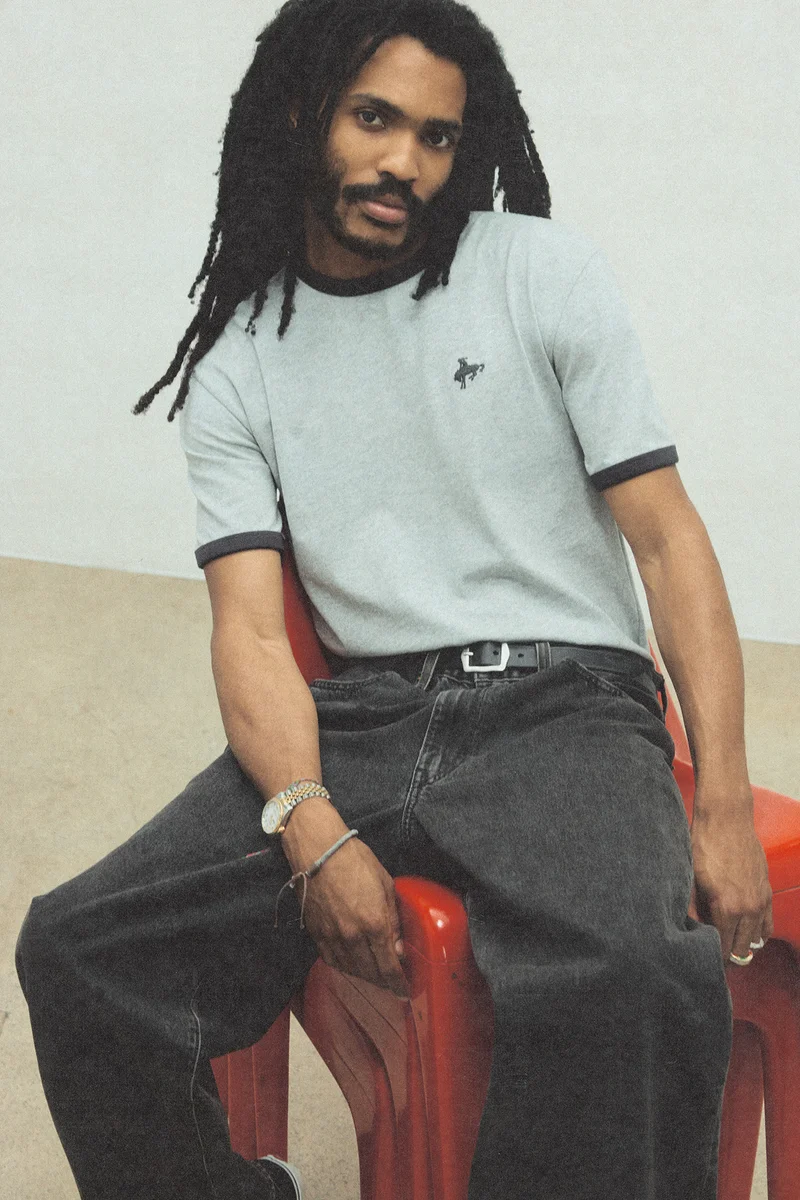 A man wearing a grey ringer tee and black jeans.