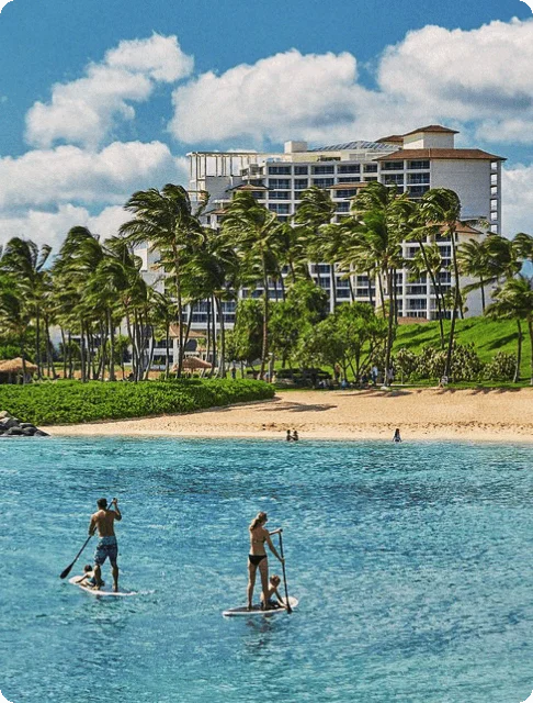 Image Description: Two travelers paddleboarding near a beach in front of Four Seasons Resort Oahu At Ko Olina