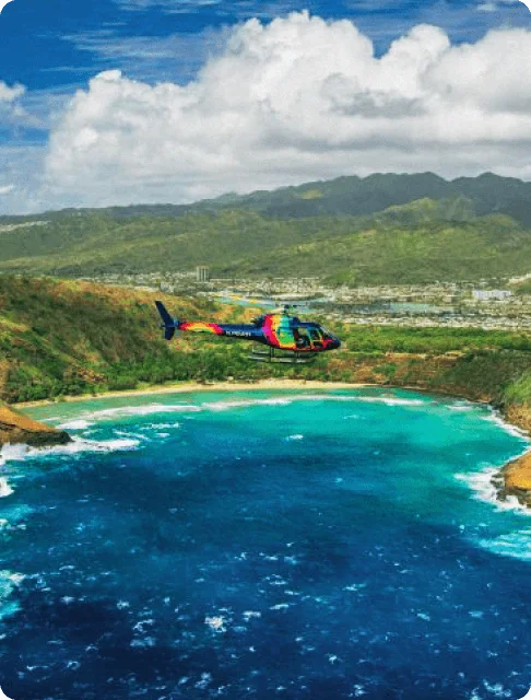 Image Description: A rainbow-colored helicopter flying over a sparkling coastline in Oahu, Hawaii