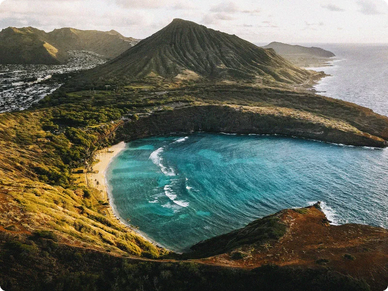 Image Description: Aerial view of a beach surrounded by rolling green hills in Oahu, Hawaii