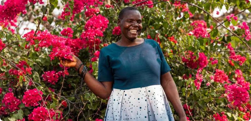 A woman smiling in front of a bright red flower bush.