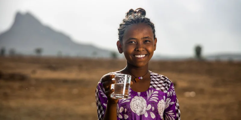 A young woman smiling at the camera holding a glass of water.