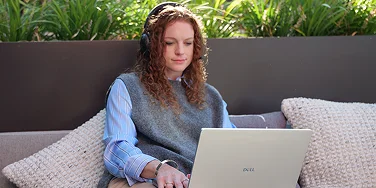 An office worker sitting on an outdoor sofa working on a Dell laptop.