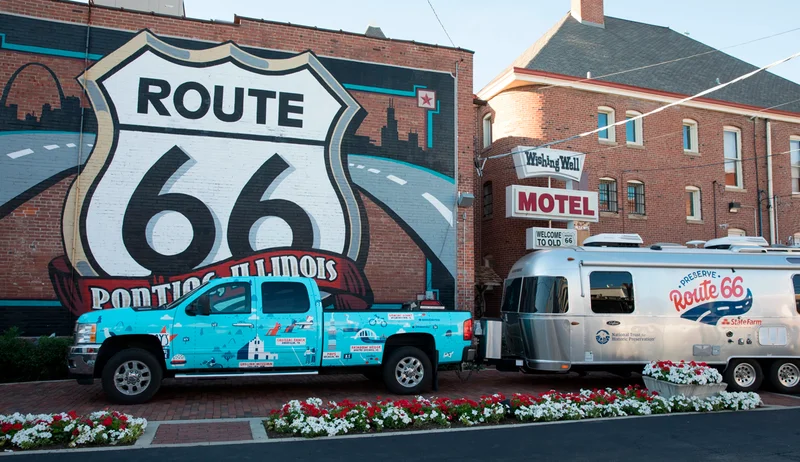 Blue pickup towing silver Airstream, Route 66 mural background.