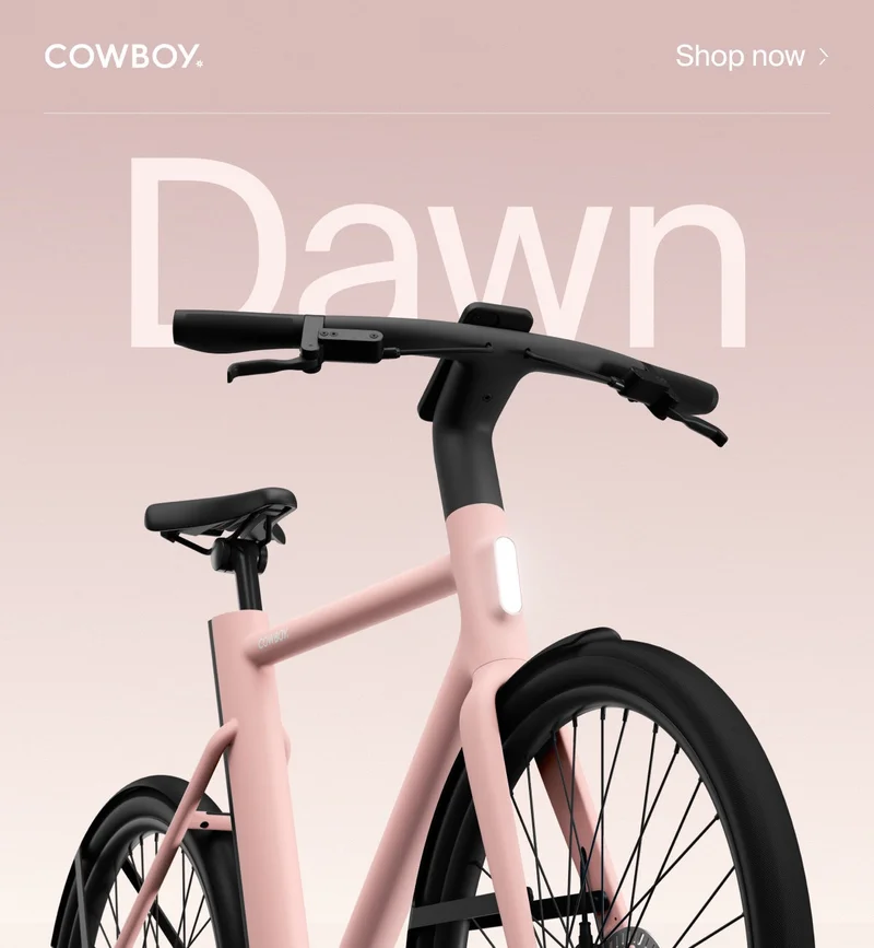 A Cowboy e-bike in the Dawn colorway, a soft pink frame with black accents, shown from a low angle against a gradient background with the word “Dawn” in large text.