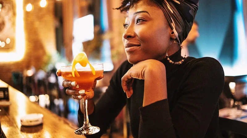 Image description: Woman having a cocktail at a bar alone.