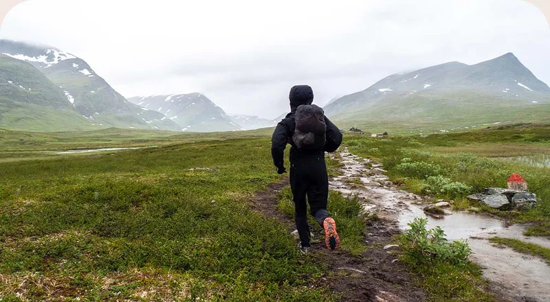 A person runs on a wet trail in the mountains of Sweden.