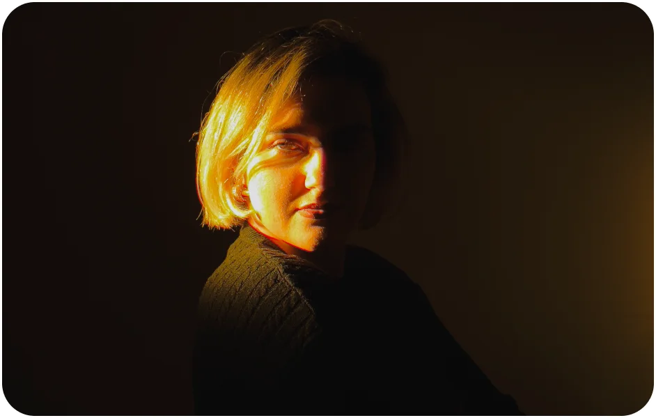 low lit image of a woman with a soft smile in a dark room.