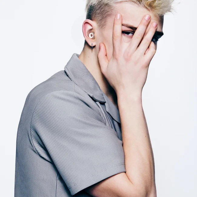 A man wearing Loop earplugs peek at the camera through his fingers