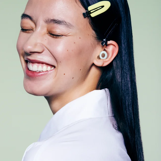 A woman wearing a pair of Loop Quiet earplugs smiles and shuts her eyes.