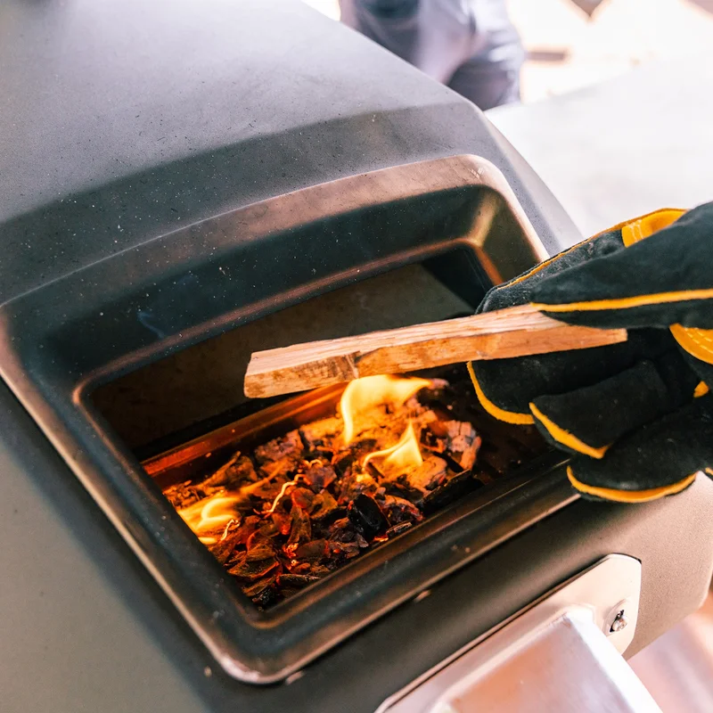 Gloved hand putting wood fuel into Karu oven
