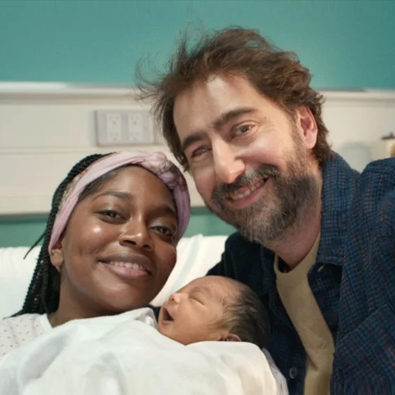 Two people smiling while holding a newborn baby