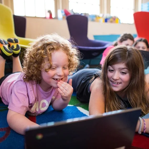 Two children smiling while using a computer