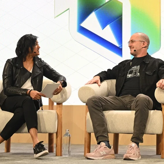 two people seated in chairs on a stage having a conversation