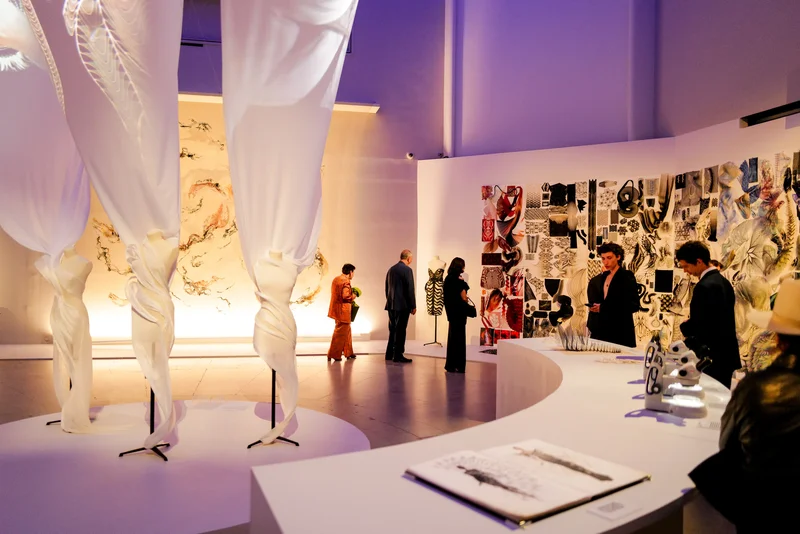 People walking around a gallery containing microscopes, dresses, vision boards, and purple walls