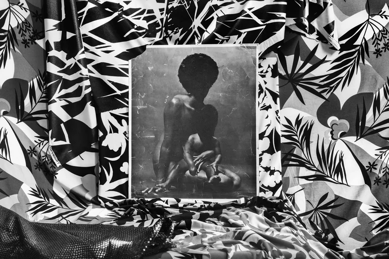A collage of a black-and-white photo of a mother and child laid over patterned fabric