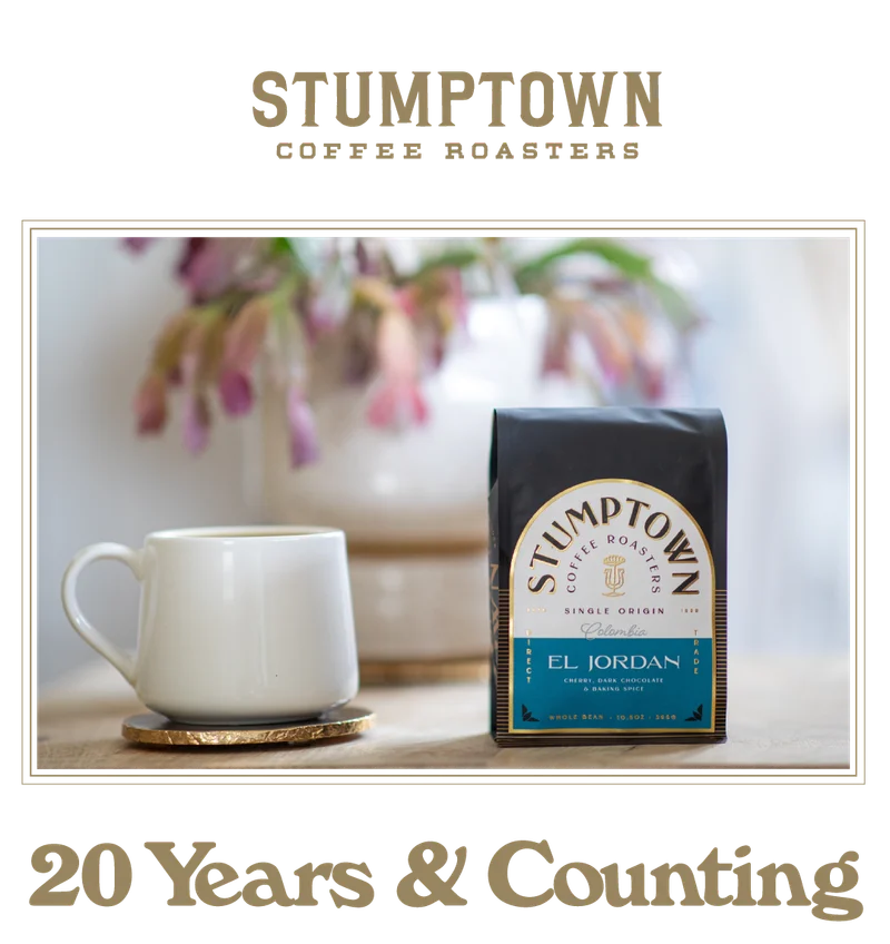 A white ceramic coffee cup on a gold coaster sits beside a bag of Stumptown Coffee Roasters El Jordan single origin coffee. Soft-focus flowers appear in the background, and the text “20 Years & Counting” is displayed below the image.