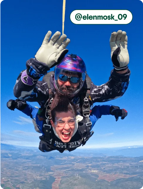 Image description: A woman and a Skydive Athens instructor smiling mid-air, photo taken by @elenmosk_09