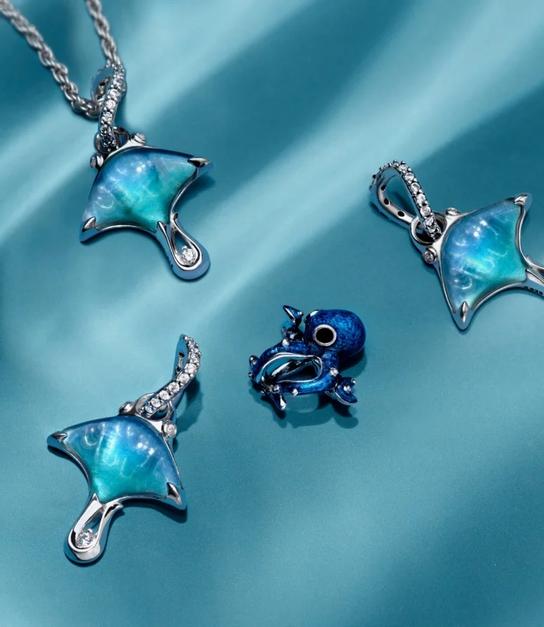 Blue manta ray and octopus Pandora Moments charms on a blue background.