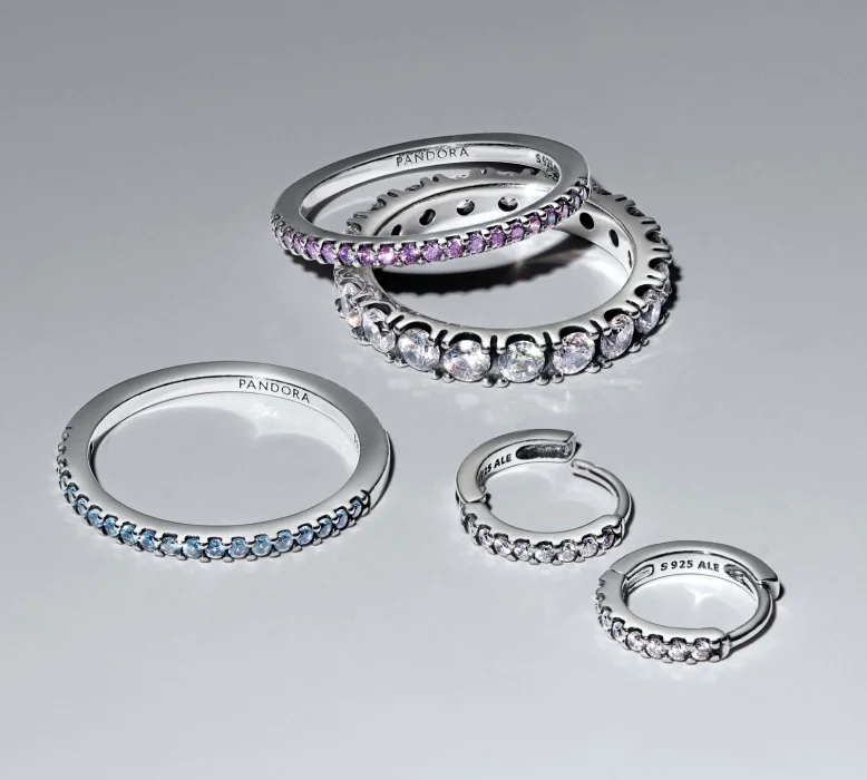 Sterling silver Pandora Timeless rings and hoops scattered on a grey background.