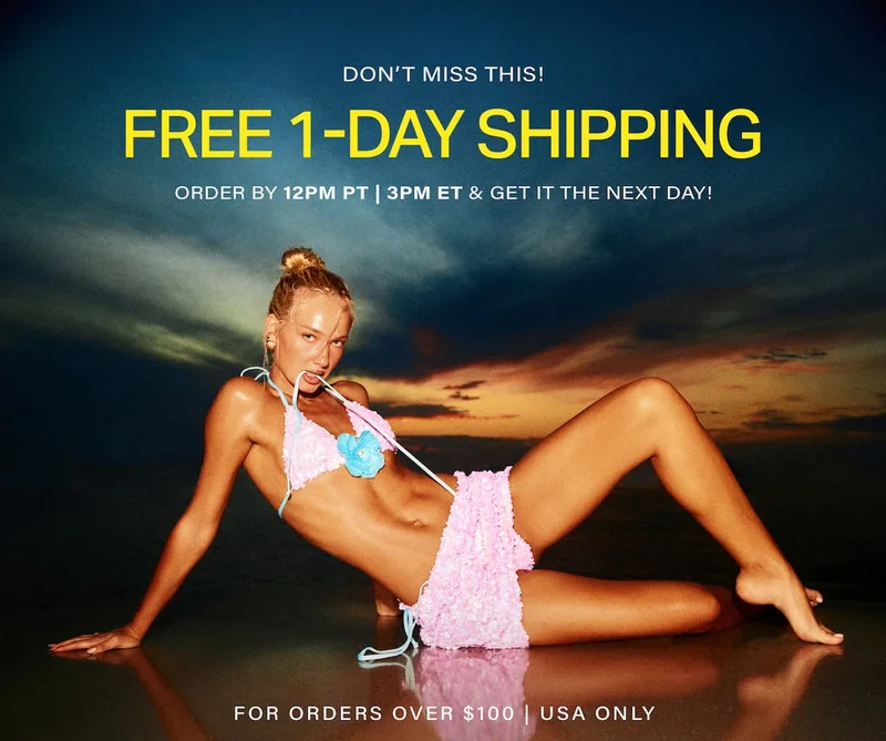 Model in a ruffled pink bikini with a blue flower reclines on a reflective shore at sunset. Get free 1-day shipping on new swimwear.