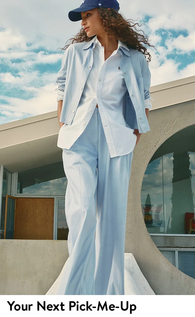A woman wearing layered button-up shirts with trousers and a baseball cap.