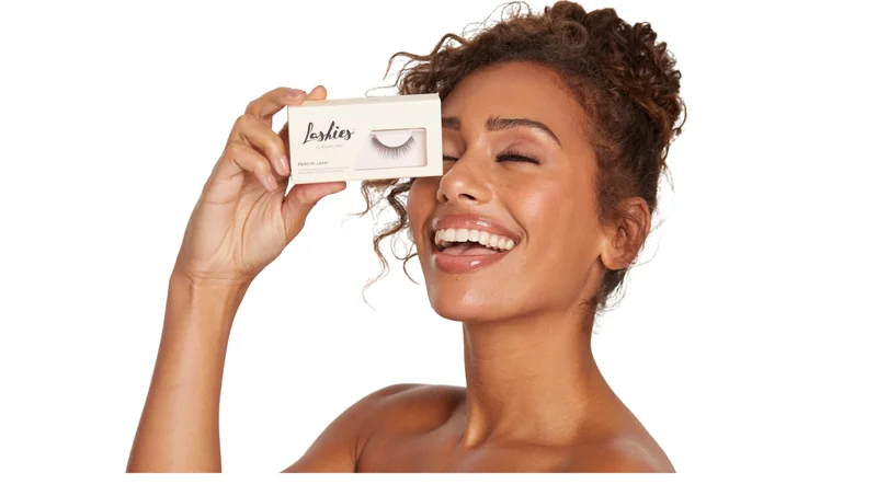 Happy woman holding Lashies false lash packaging near her eye, showcasing beautiful lashes and glowing smile