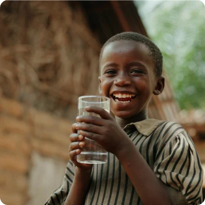 A young boy holding a glass of water and smiling.