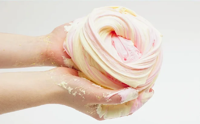 Hands squeezing pastel-colored fluffy slime.