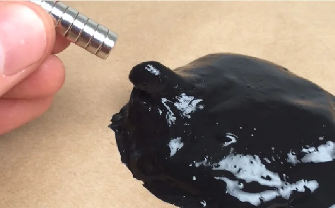 A hand holding a magnet pulling black slime upward.