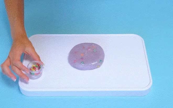 Hands stretching translucent slime with glitter over a white tray.