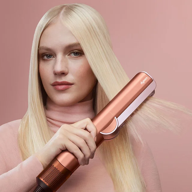 A model smooths and straightens her hair with the Dyson Airstrait dryer and straightener