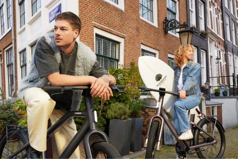 A pair friends standing with their Cowboy bikes in a city setting.