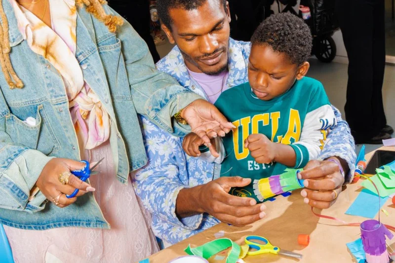 Two adults and a child making art with colorful paper and scissors