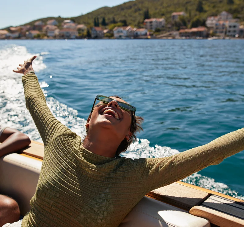 A happy woman on a boat with her arms raised in the air