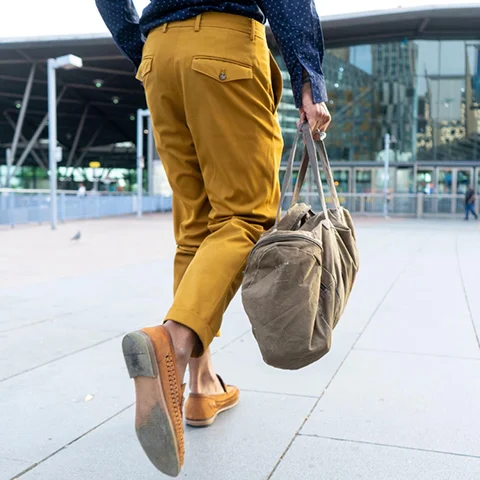 A man with brown shoes and a brown bag walking on a city street.