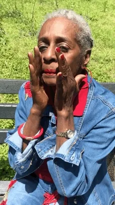 An older Black woman smoothes skin care on her face.