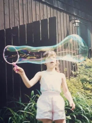A child has a look of awe while they make a large bubble across their face.