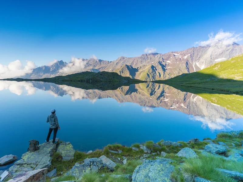 Rear view of hiker on rocks admiring Cima di Pietra Rossa reflected in Lago Nero, Gavia Pass, Valfurva, Valtellina, Lombardy, Italy.