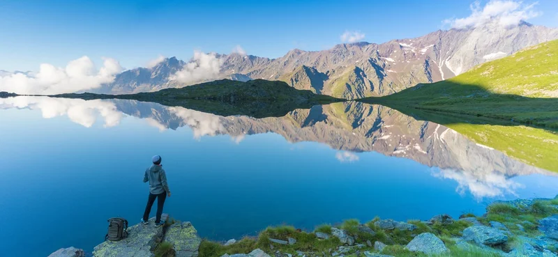 Rear view of hiker on rocks admiring Cima di Pietra Rossa reflected in Lago Nero, Gavia Pass, Valfurva, Valtellina, Lombardy, Italy.